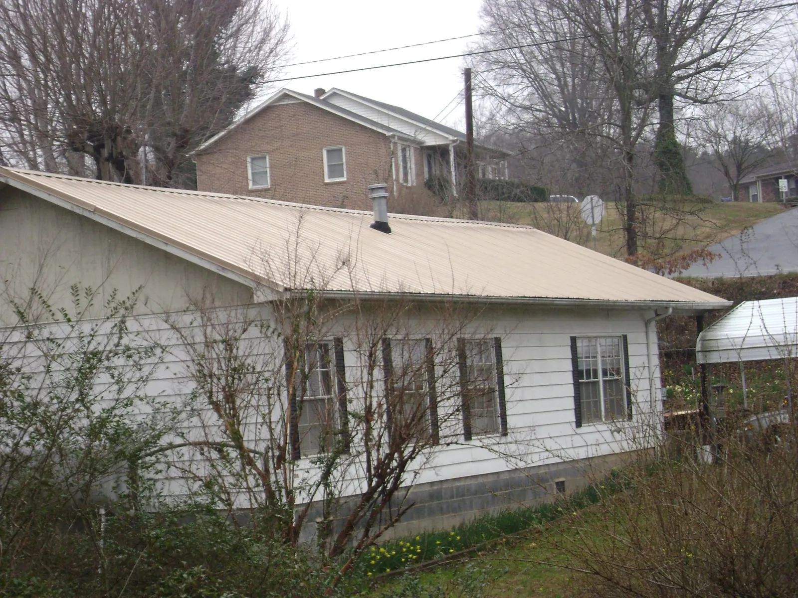 Tan metal roof on a white sided house set into a hillside — Commercial Roofing by Roofing Brothers in Riverdale